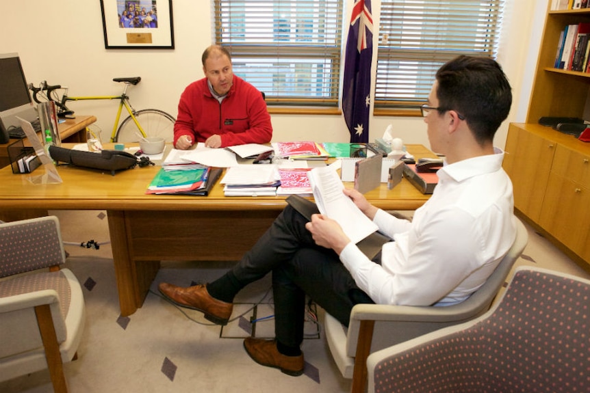 Josh Frydenberg meets with a staffer in his office while wearing his exercise attire.