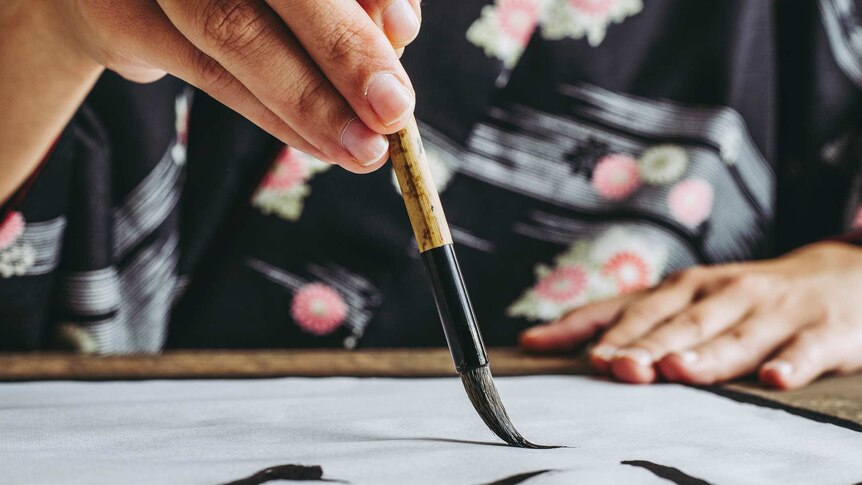 female hand holding calligraphy brush composing on paper