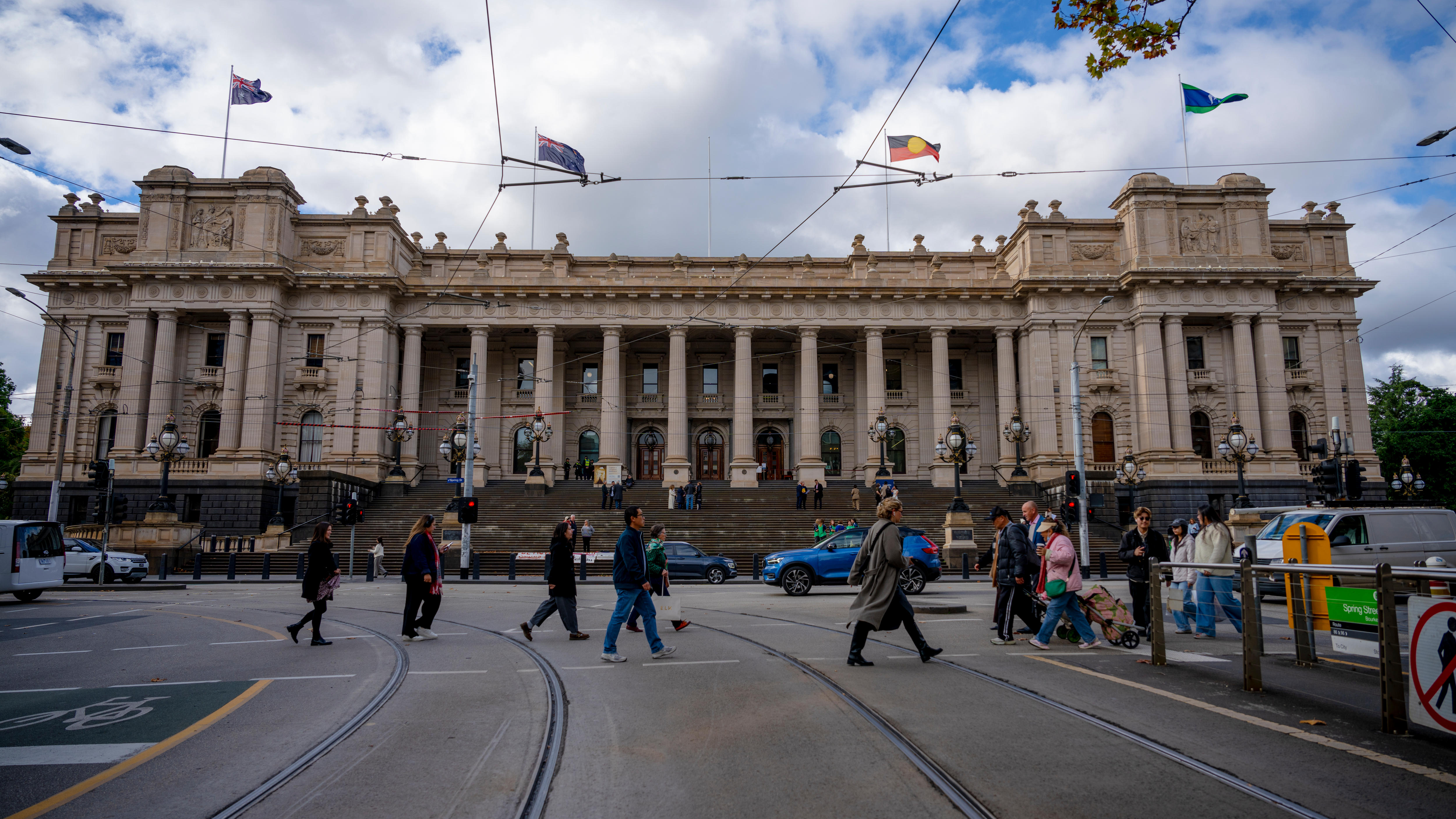 People cross a road in front of the Victorian parliament building in Melbourne.
