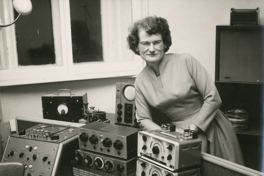 Black and white archival photo showing 40-something-year-old woman in BBC sound studio surrounded by gear.