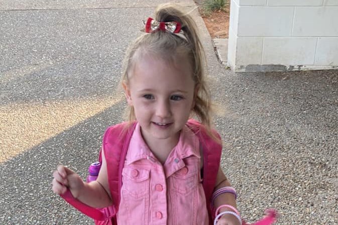 A little girl wearing a backpack smiles at the camera.