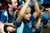 A young girl raises her hands above her head in a classroom