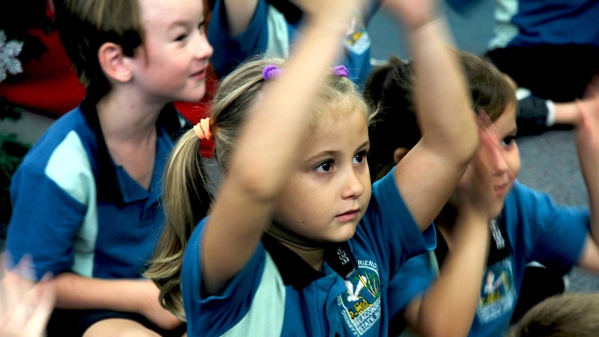 A young girl raises her hands above her head in a classroom