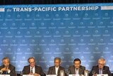 The twelve Trans-Pacific Partnership Ministers sit at a long table while holding a press conference.