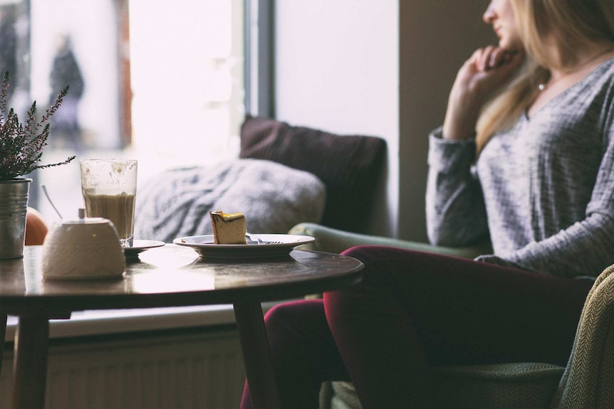 Woman sitting in a cafe with her head turned out the window to depict what to do when you feel lonely during holiday season.