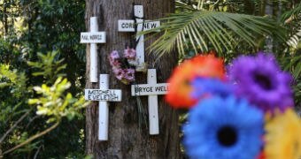 Four crosses are nailed to a three with coloured flowers in roadside tribute.