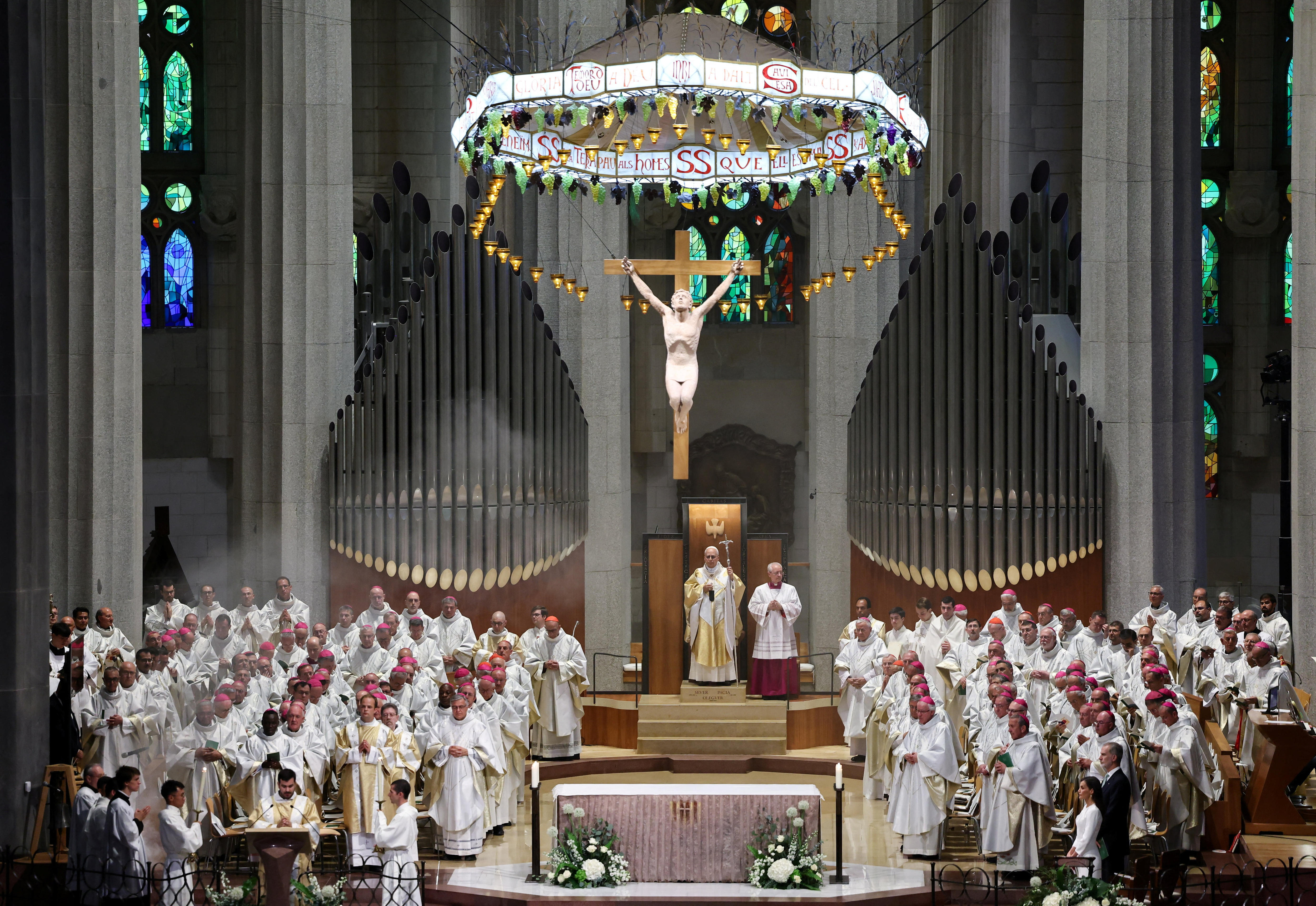 Pope Leo and Catholic Church clergy members in white and gold robes standing under large organs and a sculpture of Jesus.
