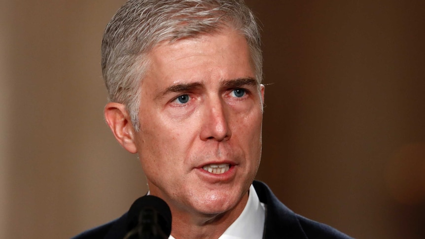 Close up of Neil Gorsuch in a suit speaking into a microphone