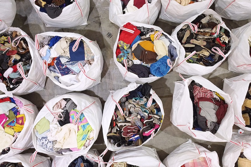 Bags of textiles to be recycled sit open on a concrete floor.