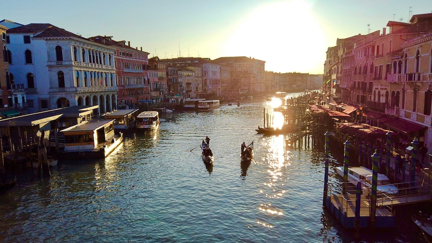 A wide canal with two gondolas and setting sun.