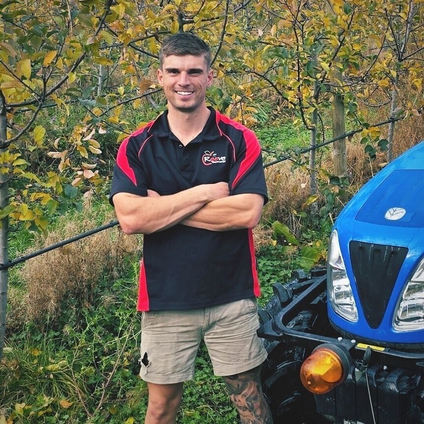 A young fruit grower standing alongside his tractor on a Huon Valley orchard