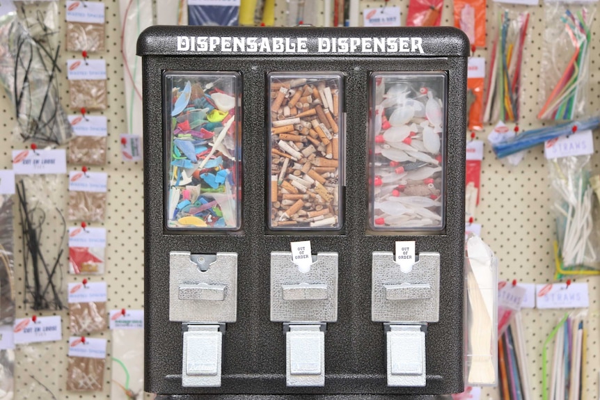 An art piece designed to look like a coin-operated lolly dispenser, filled with rubbish and labelled 'dispensable dispenser'.