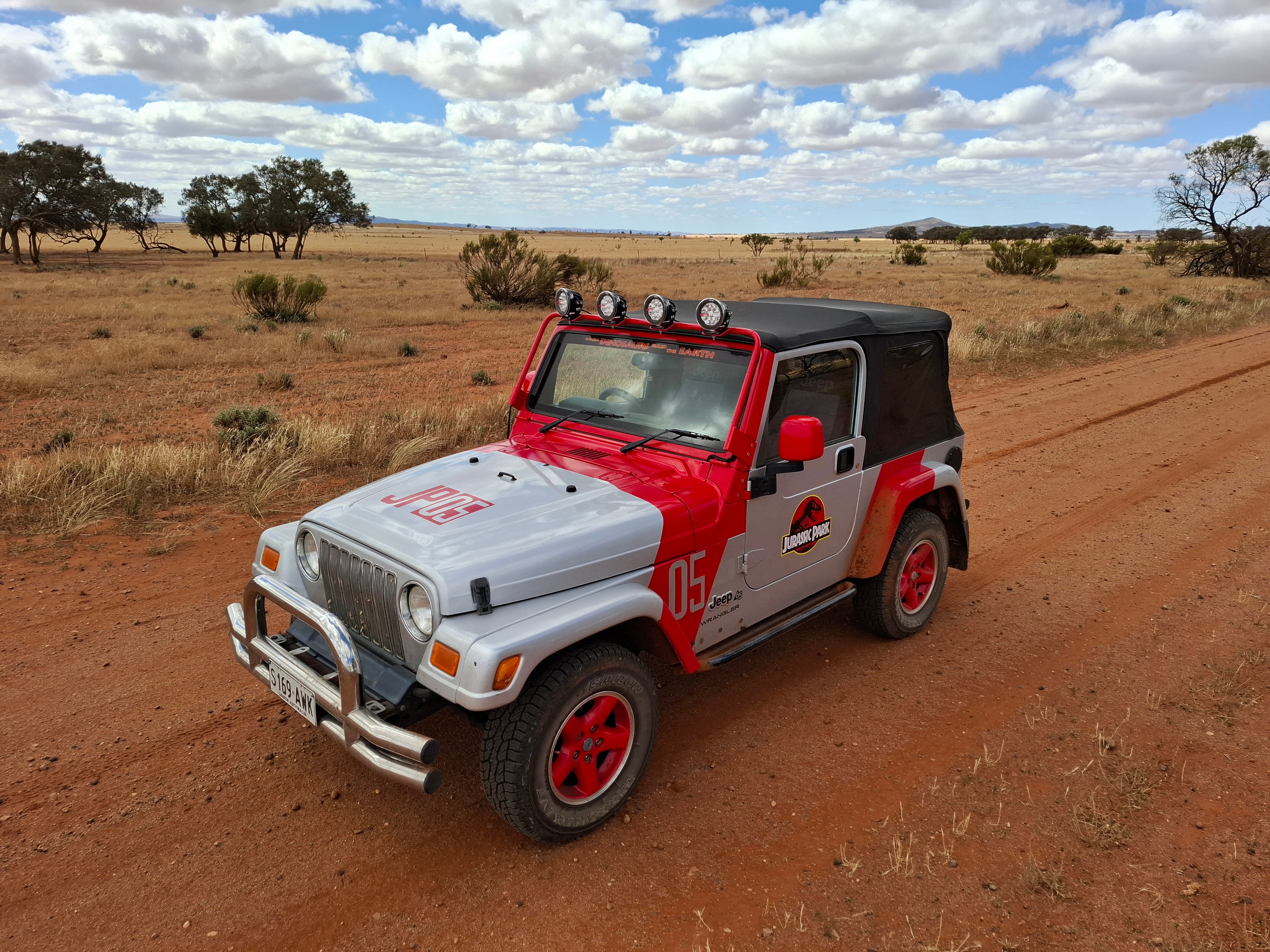 Un jeep rojo y gris con el logo de Jurassic Park en la puerta en una carretera del interior