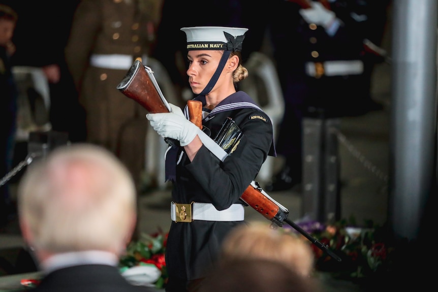A woman in a navy uniform carries a gun.