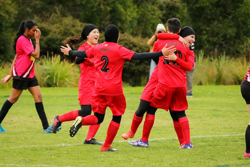 team members in red hug and celebrate at a football match in Melbourne