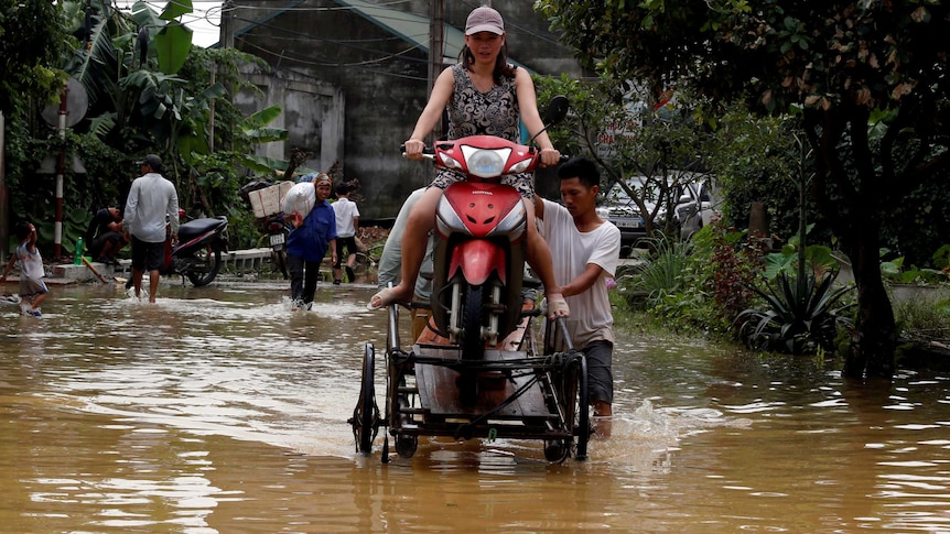 A woman sits on a scooter as men push her through floodwaters.