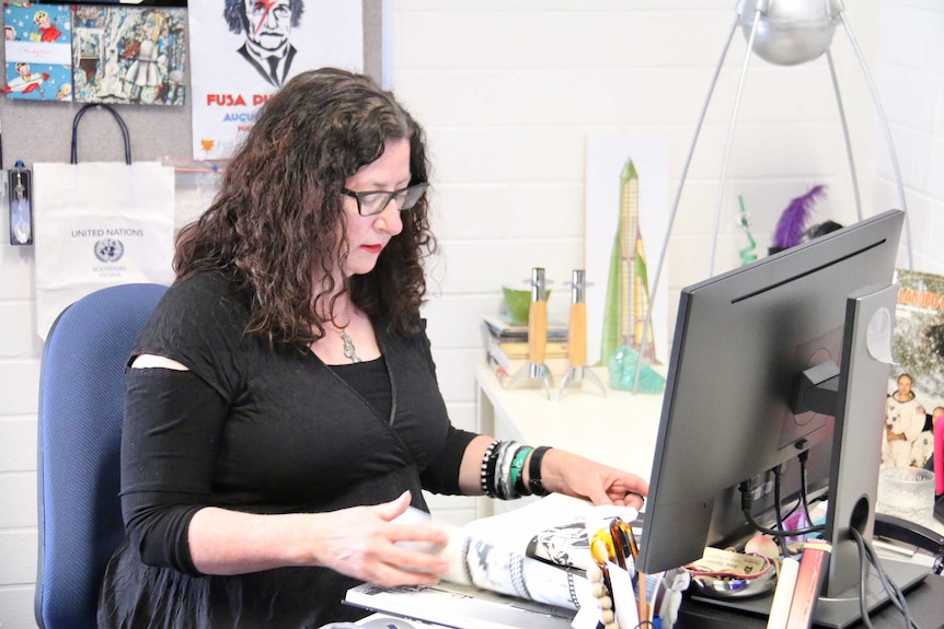 A woman sits at a desk in front of a computer.