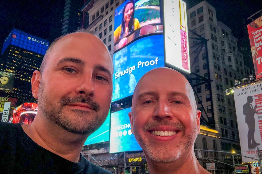 Two men standing in front of the large billboard in Time Square.