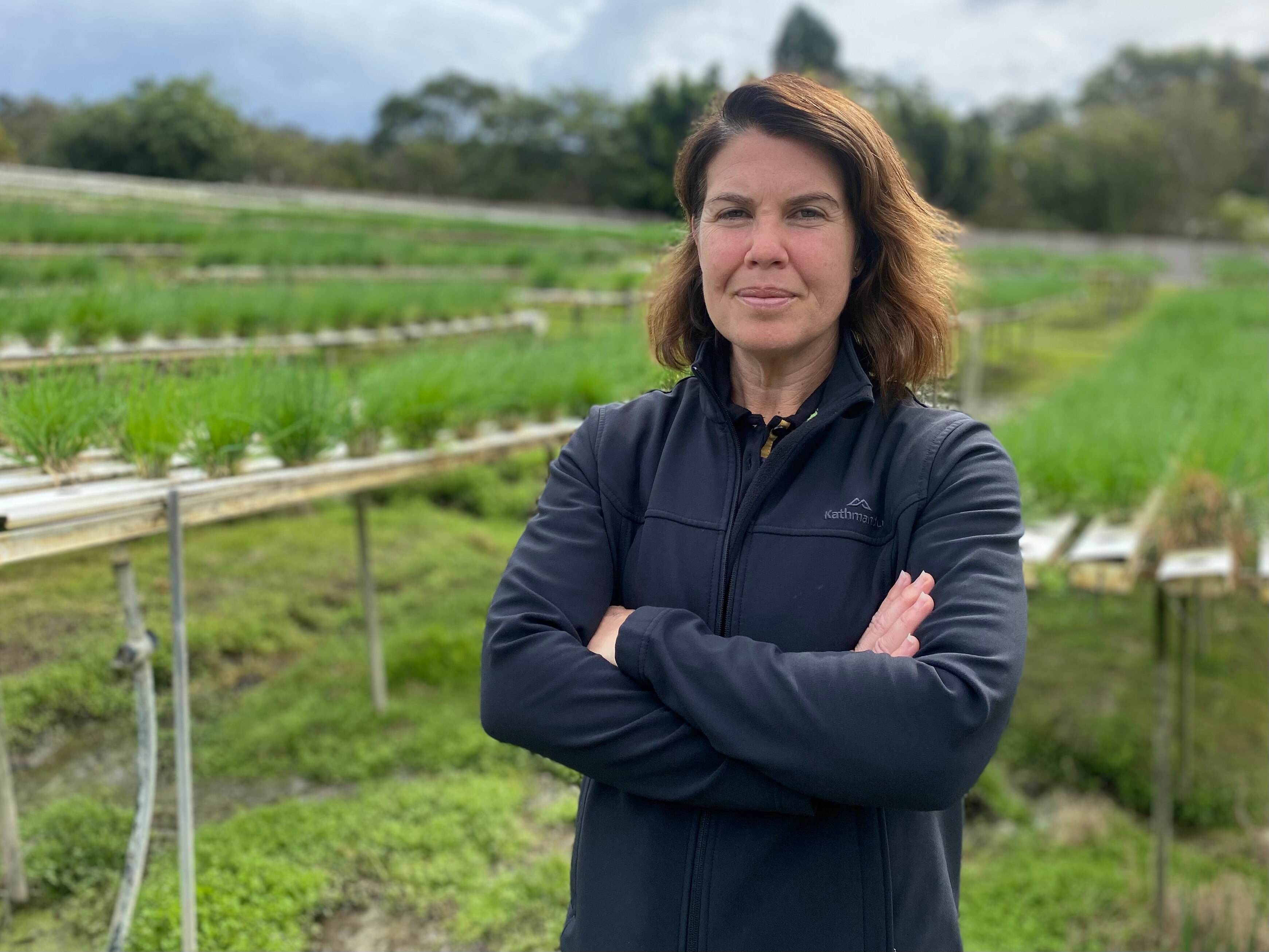 Woman stands with arms crossed and lettuce growing behind her