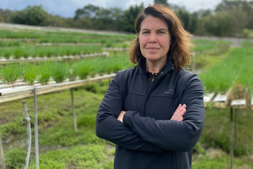 Woman stands with arms crossed and lettuce growing behind her