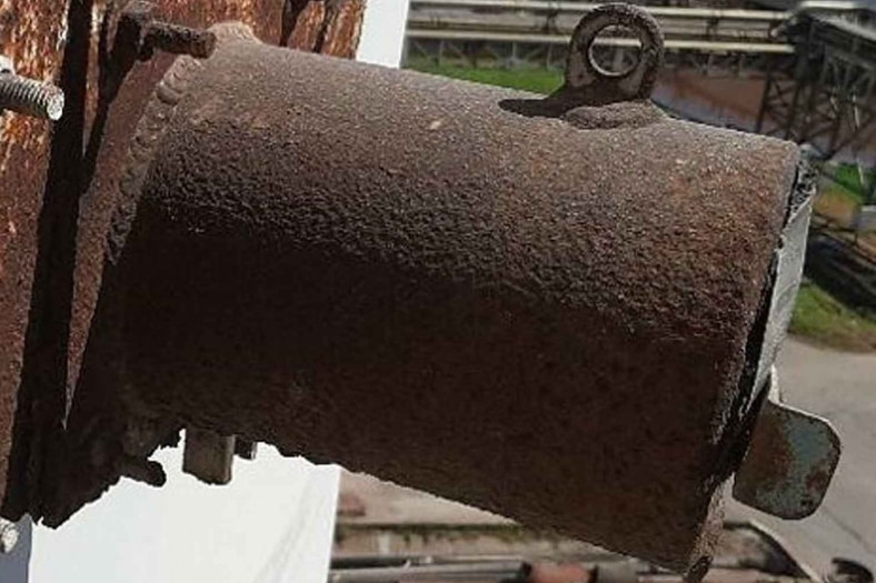 A rusty grey-ish brown metal tube protrudes from an exterior wall.