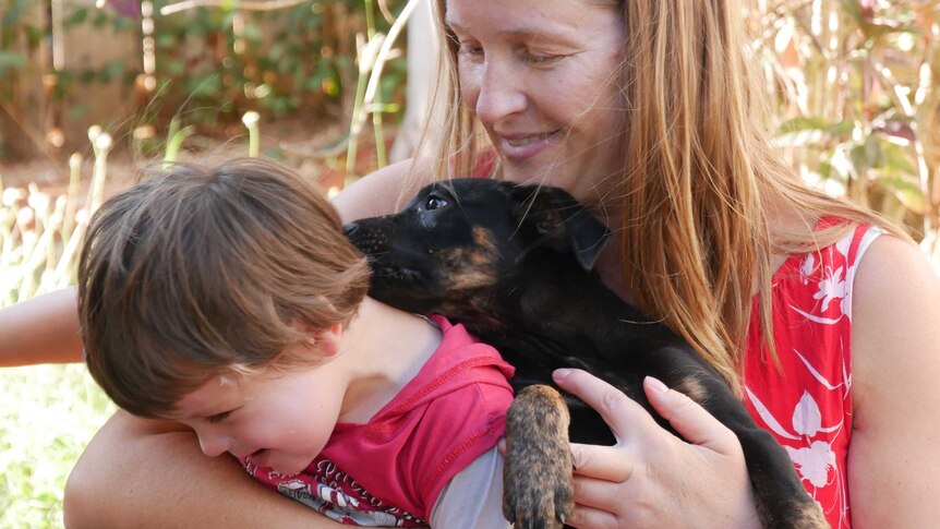 A boy cuddles a puppy with his mother.