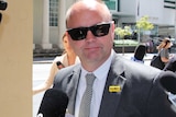 A head and shoulders shot of former state Labor MP Barry Urban wearing a suit and sunglasses outside court, with media in tow.