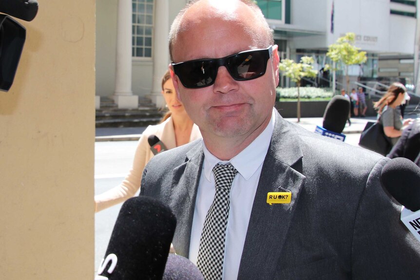 A head and shoulders shot of former state Labor MP Barry Urban wearing a suit and sunglasses outside court, with media in tow.