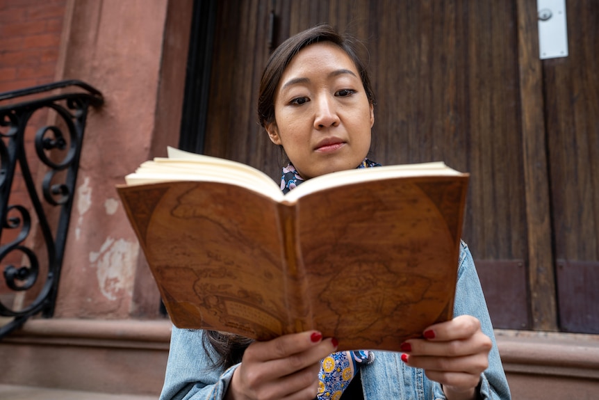 Woman reads a book on the steps of an apartment building.