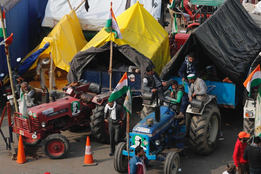 People sit on tractors, which have been parked in front of traffic cones on the street