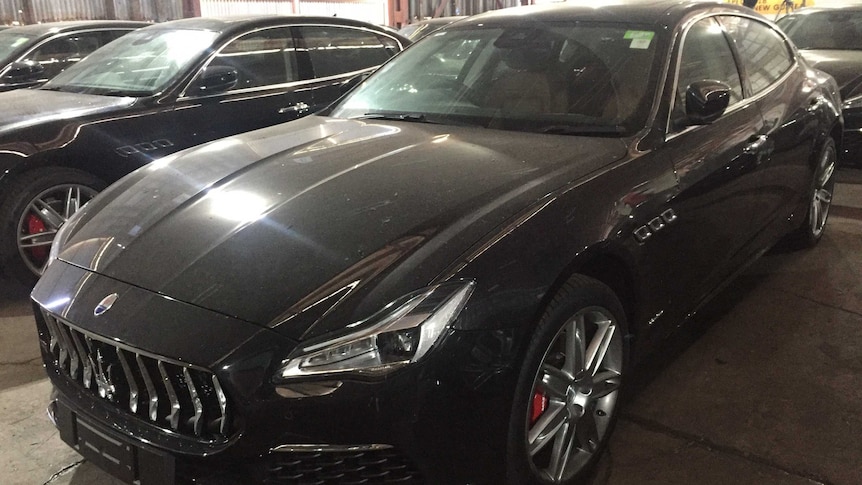 A row of black Maserati's sit in a shed.