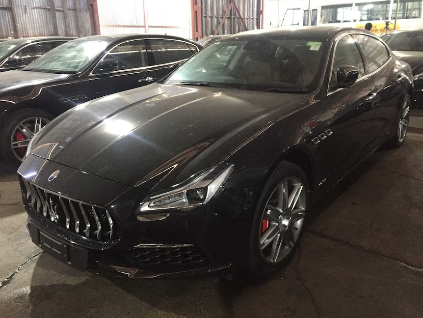 A row of black Maserati's sit in a shed.