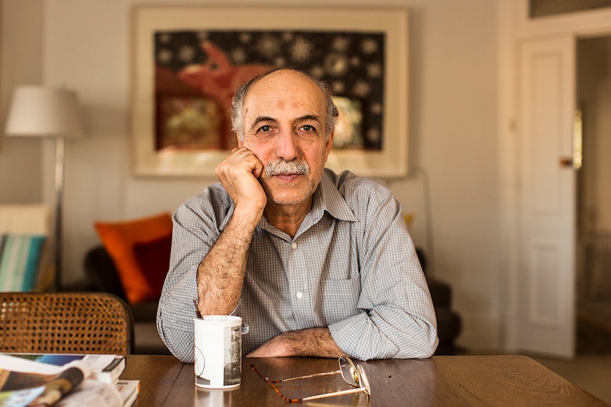 Colour photo of former Woomera Detention Centre detainee and asylum seeker Hassan Sabbagh sitting at table in living room.