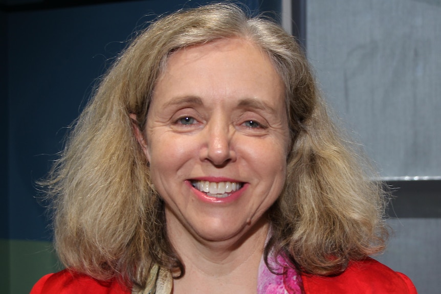 A woman with blonde hair smiling in a red blazer.