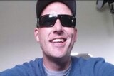 A man in his 30s, wearing sunglasses and a cap, smiles in a selfie-style picture.