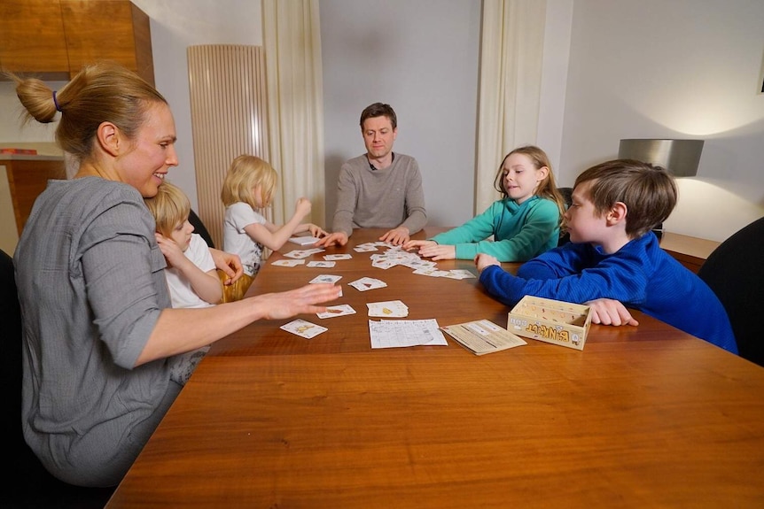 Adam Zych sits at the head of a table surrounded by four children and a woman, all children's playing a card game