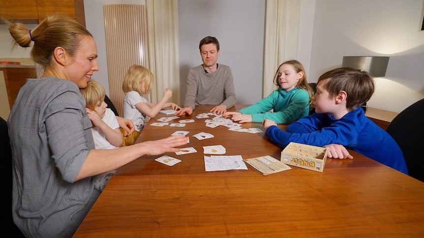 Adam Zych sits at the head of a table surrounded by four children and a woman, all children's playing a card game