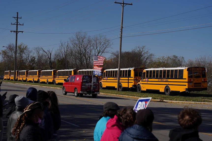 A red van flying Donald Trump flags drives past supporters of presidential rival Joe Biden at an election rally in Michigan.