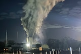 Large smoke plume rising into dark sky from coal mine