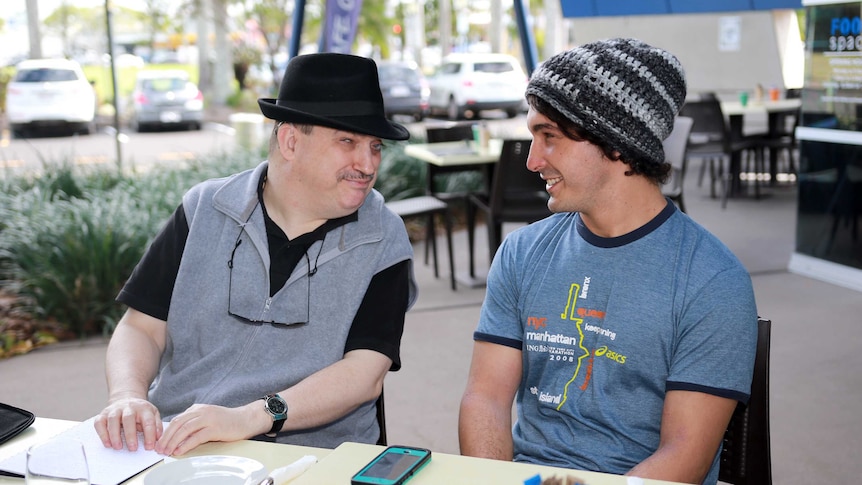 Two men smiling at each other at a cafe