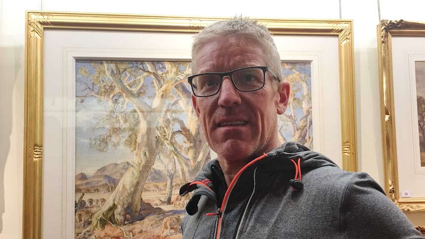 Jason Duffield smiles in front of his new painting - a Hans Heyson watercolour of the bush