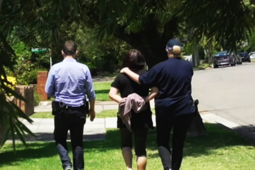 Police can be seen leading a woman down a suburban street.