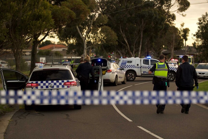 Police tape cordons off a crime scene, with police cars and officers seen on a suburban street.