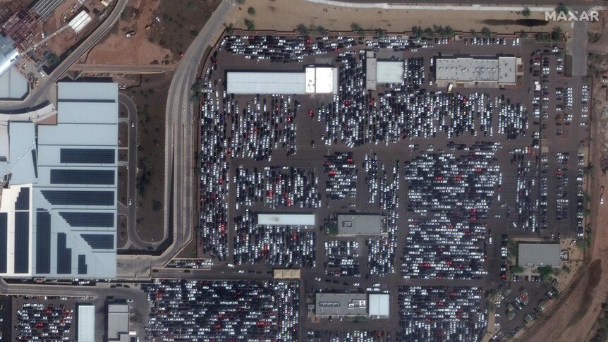 A satellite image shows hundreds of idle rental cars parked in a lot outside Phoenix Airport in Arizona