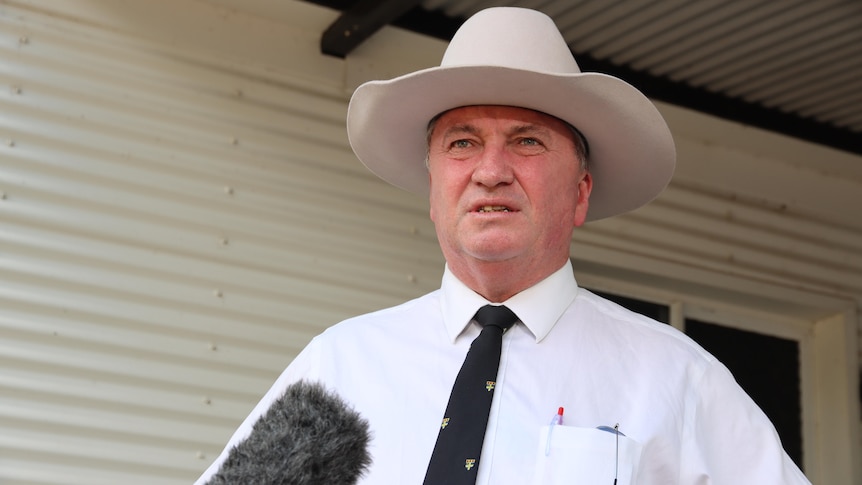 A man wearing an akubra hat speaks at a press conference in front of an outback building