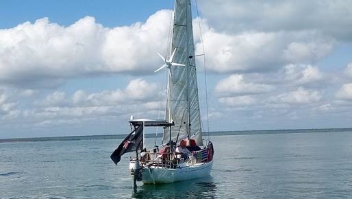 A yacht is seen floating in the sea in the middle distance with a flag and people aboard.