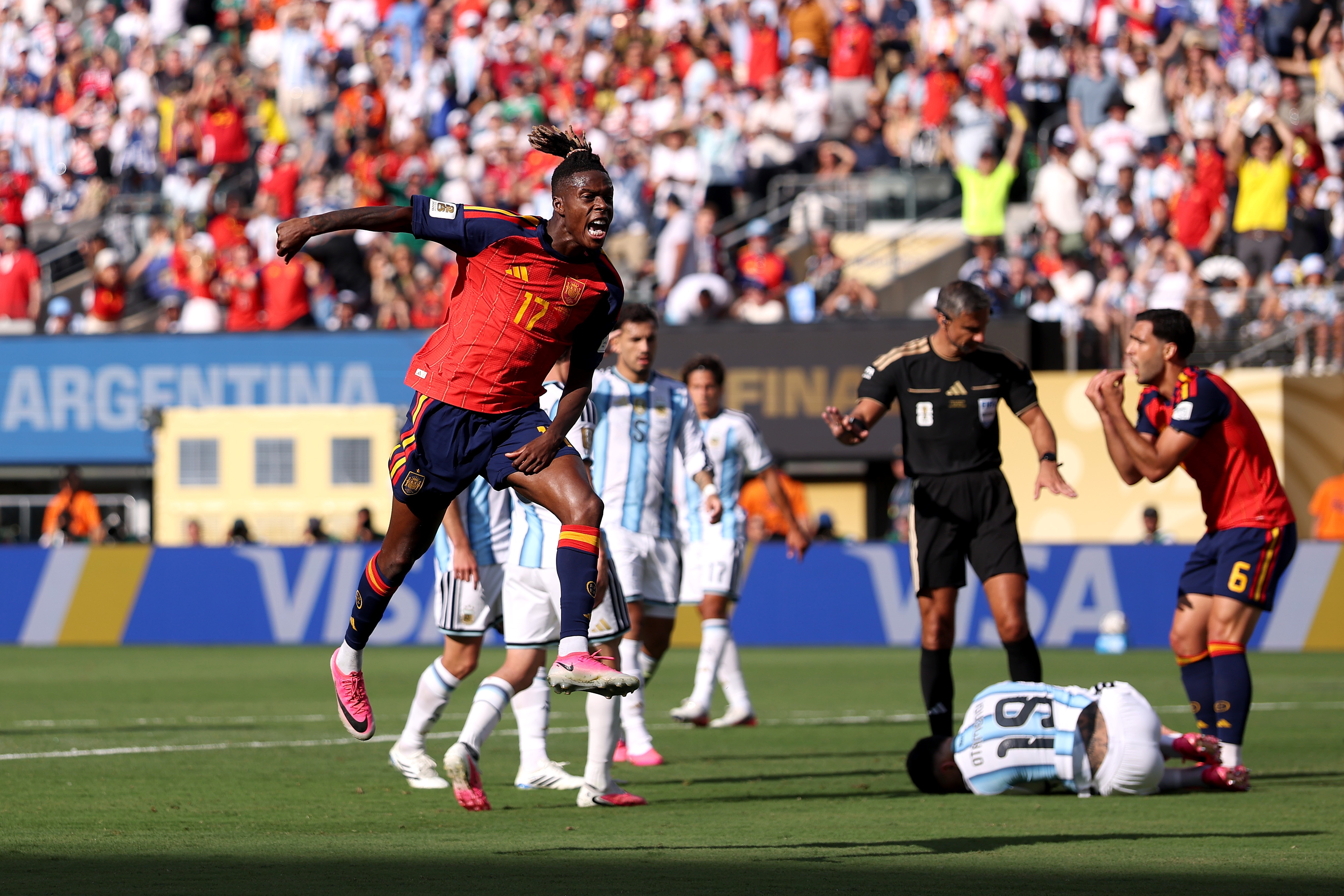 A black man in a red jersey leaps into the air in front of several soccer players.
