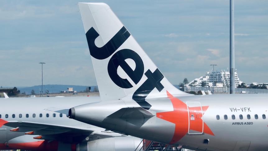 The tail of a Jetstar plane with its logo parked at an airport on a sunny day.