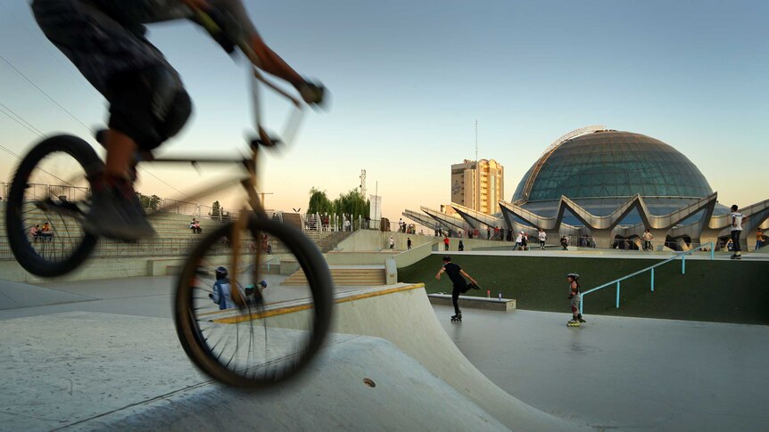 A BMX bike is blurred in the foreground at a skate park next to a big dome.