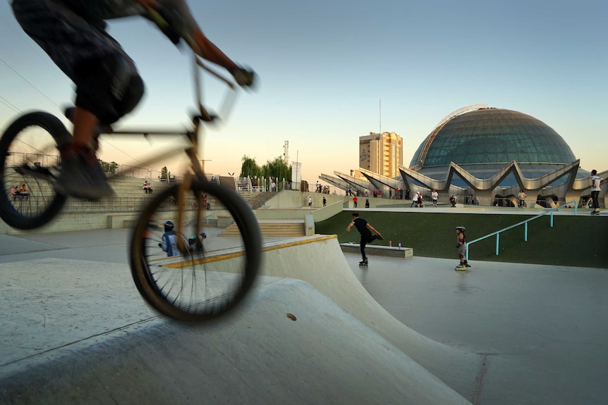 A BMX bike is blurred in the foreground at a skate park next to a big dome.